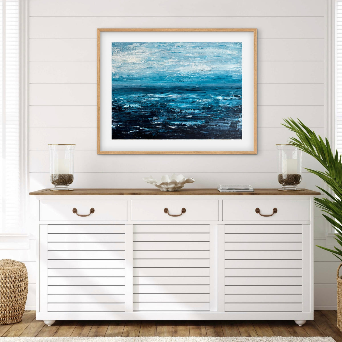 Quiet Tide framed print displayed above a white console with a plant in a light coastal room